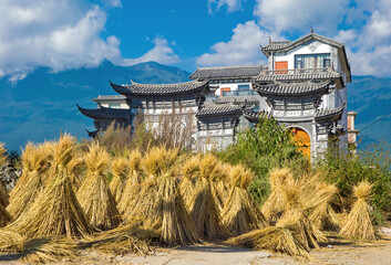 Landanwesen in China n&auml;he Ohrensee. Im Vordergrund angeh&auml;ufte Stengel von der Reisernte. Bauernof in typiscen Baustil. Landwirtschaft, Ernte, Reis, Haus.