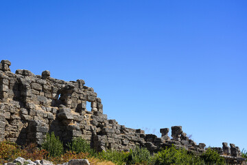 Fototapeta premium Ancient Stone Ruins Under a Clear Blue Sky Highlighting the Remnants of a Historic Civilization Surrounded by Greenery and Natural Beauty