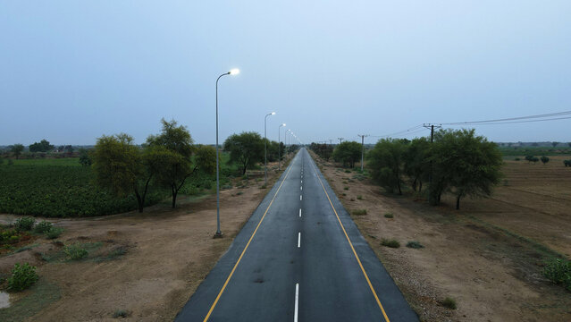 An empty asphalt road, with street lights on, in the middle of a desert