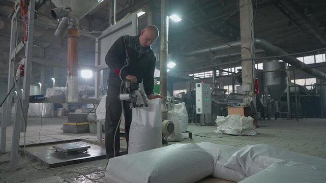 Factory worker using a handheld tool to seal the sacks with produced material. Factory worker stacking multiple sacks on a wooden pallet. Factory worker storing the sacks full of pellets.