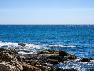 Breathtaking Coastal Scene Featuring Rocky Shoreline with Clear Blue Waters Under a Sunny Sky and Gentle Waves Lapping at the Rocks