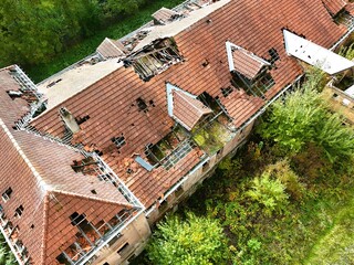 Aerial view of abandoned building with collapsed roof surrounded by forest