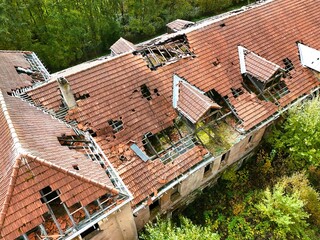 Aerial view of abandoned building with collapsed roof surrounded by forest