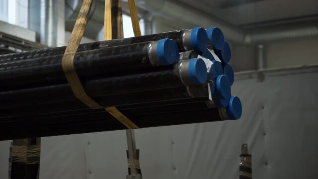 Factory crane equipment lifting the produced metal tubes from the conveyor. Factory crane picking up the steel tubes. Factory crane moving the tubes to a different section. Production process.