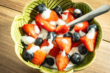 A green bowl of yoghurt with Strawberries and blueberries.