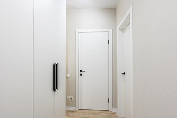 Minimalist interior featuring white walls, two doors, and a wardrobe. The color scheme is predominantly white