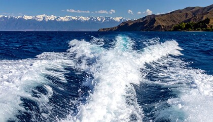 Sparkling wake on a serene lake.  Mountains and snow