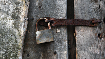 old padlock. Closeup view of an old padlock covered in rust, attached to a cracked wooden door. It represents themes of security, the passage of time, decay, and vintage aesthetics. the door is locked