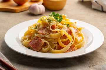 Creamy fettuccine pasta with bacon and carbonara sauce topped with parsley and parmesan cheese in a plate.