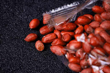 Freshly shelled peanuts scattered on a dark surface with a plastic bag partially open displaying...