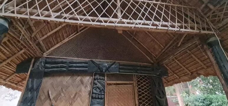 A traditional indigenous bamboo and thatch hut from North East India on display at the National Crafts Museum in Delhi, featuring tribal motifs and woodwork.