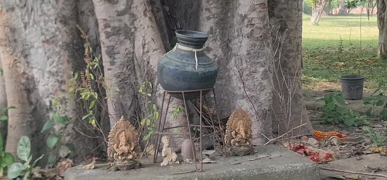 Sacred Religious Shrine Featuring Clay Idols and a Traditional Matka Near an Ancient Tree Root