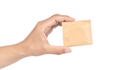 Close-up of a hand holding a small, square, tan packet against a black backdrop