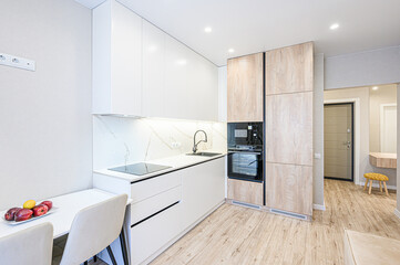 Modern kitchen with sleek white cabinets, marble-effect backsplash, and wood-toned accents. Includes a built-in oven, stovetop, and a small dining area