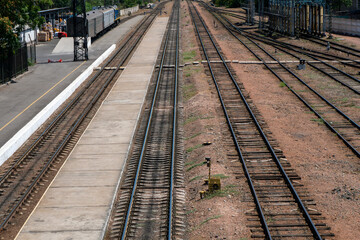 Obraz premium Mainline tracks, side tracks, concrete platform, turnout mechanisms, signal box, semaphore, overhead gantry, catenary supports. Stationary passenger coaches, operational railway yard environment