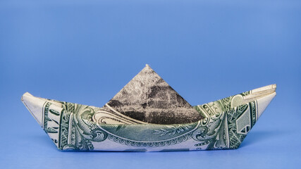 Creative craft using a dollar bill folded into a boat shape on a blue background