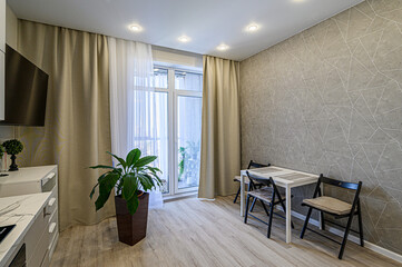Cozy kitchen-dining space with a white table, chairs, curtains, geometric wallpaper, and a large potted plant by the window