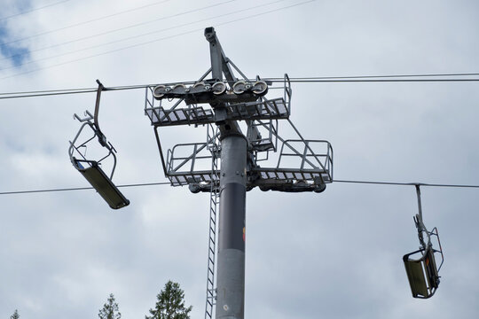  ski lift or chairlift pylon with its complex wheel mechanism and support structure, set against a bright, cloudy sky, suggesting off-season mountain tourism. - Powered by Adobe