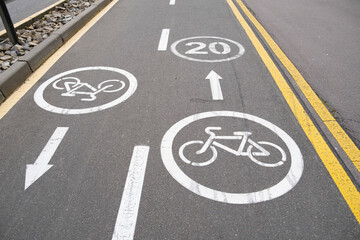 Fototapeta premium Bicycle lane markings, including bike symbols and a 20 km/h speed limit, painted on a gray asphalt road surface with yellow divider lines, indicating a two-way bike path.