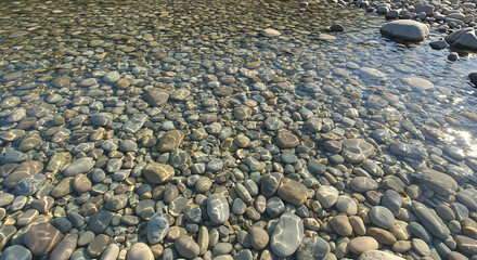 View from above of small rounded stones visible beneath the clear flowing river water. Gentle light distortion creates natural movement patterns.