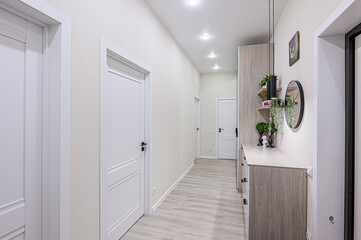 A well-lit hallway with light wood floors, white walls, and doors. A console table with decorations and a mirror adds style