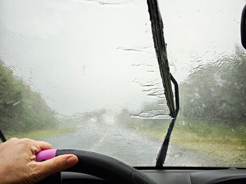 Driving through heavy rain on a foggy road with limited visibility and windshield wipers working hard to clear water - Powered by Adobe