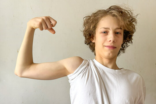 Confident Teen Boy Flexing Arm Indoors During Daytime For Concepts Of Body Positivity, Self-Esteem, Youth Identity, Physical Growth, And Empowering Visuals For Mental And Emotional Strength Campaigns