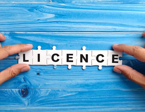 Hands placing a jigsaw puzzle spelling "LICENCE" on a blue wooden surface