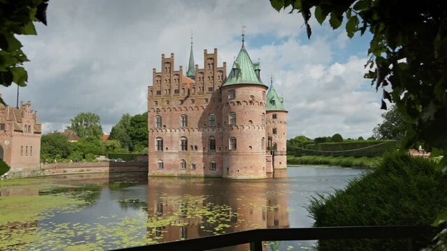 Gimbal shot of Egeskov Castle, Denmark. Egeskov Slot in Denmark - stunning Renaissance castle surrounded by lush gardens and serene waters on beautiful sunny day