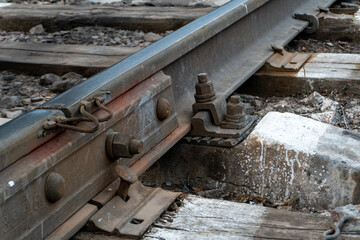 Railway infrastructure - metal rail, bolts, fasteners, wooden sleepers, gravel, and concrete, emphasizing construction, durability, engineering, and transportation elements in a rugged environment