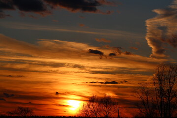 Fiery sunset sky ablaze with orange, gold, and deep red hues. Dynamic cloudscape with silhouetted...