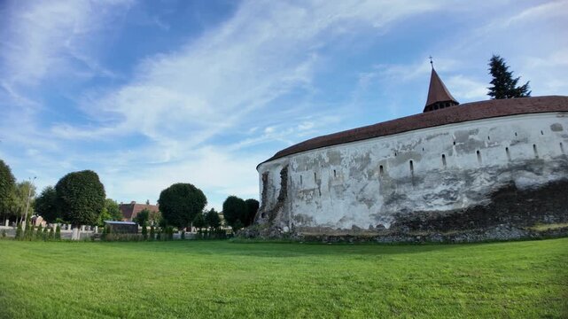 Prejmer Fortified Church in Transylvania, Romania, with massive medieval stone walls, towers and steeple under a bright blue sky. UNESCO site of Romania