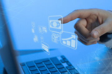 Hands interact with digital financial icons on a laptop in a modern workspace during the daytime