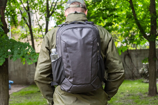 A man with a backpack, rear view. A man in a park with a city backpack. - Powered by Adobe