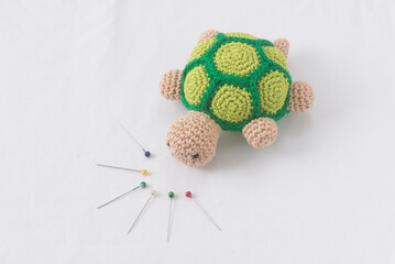 Crocheted Turtle with Pins on White Background, Intricate and Playful