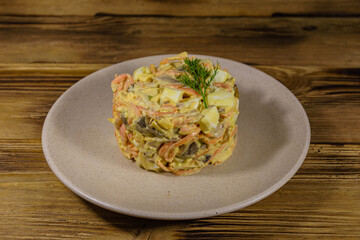Salad with chicken breast, marinated mushrooms, carrot, eggs, boiled potato and mayonnaise on a wooden table
