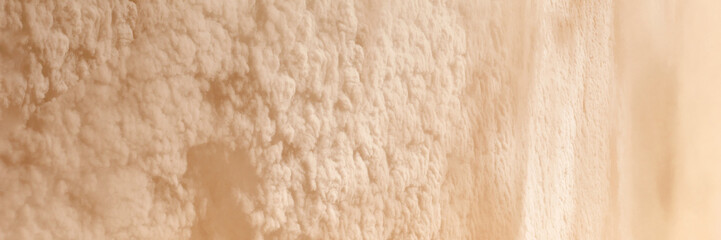Abstract textured wall surface with beige and cream rough patterns in natural light.