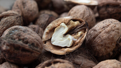 A close-up of a walnut half on a pile of whole walnuts The scene features a pile of whole walnuts in their brown shells, showcasing their natural texture.