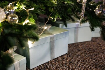 Wrapped gifts sit under a Christmas tree, surrounded by festive decorations and twinkling lights in a cozy setting.