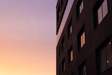 Bright hues of sunset cast reflections on sleek apartment windows in a lively cityscape during evening hours.