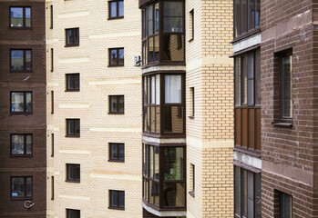 Fototapeta premium Brick apartment building with windows and balconies. Affordable housing, apartment building view. Brown brick urban housing.