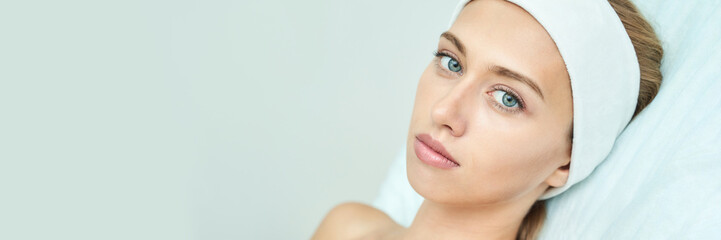 Young caucasian female with headband relaxing during spa day on white background.
