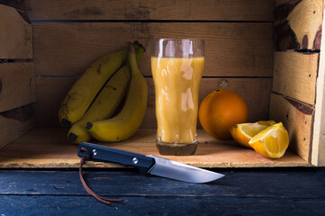 Still Life with Knife, Sliced Citrus, Bananas, and Glass of Freshly Squeezed Juice in a Crate.
