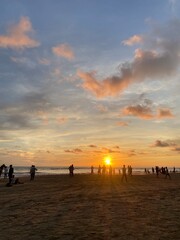 Silhouettes of beach vendors and people walking along the shore during a beautiful sunset at sea. Warm orange sky, calm waves, and peaceful seaside evening vibes.