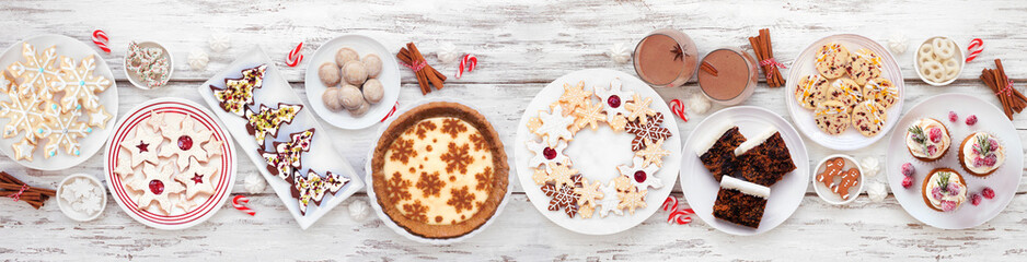Christmas holiday cookies and desserts table scene. Overhead view on a white wood banner background. Eggnog pie, a variety of cookies, fruit cake, cupcakes and chocolate eggnog.