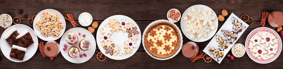 Christmas holiday cookies and desserts table scene. Top view on a dark wood banner background....