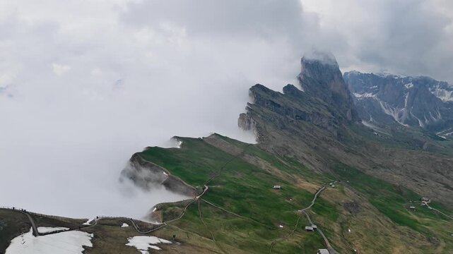 Seceda ridge transitioning to alpine meadows, aerial view. Dolomite highlands with low cloud cover and intermittent fog