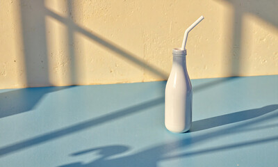 lone white bottle straw sits blue surface surrounded warm sunlight casting long golden