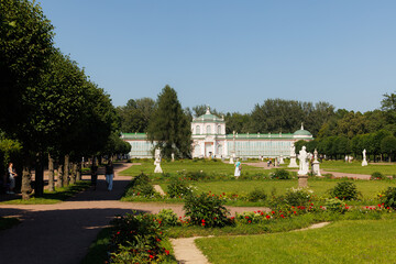 Visitors stroll through a vibrant garden featuring sculptures and historic buildings under a clear blue sky.