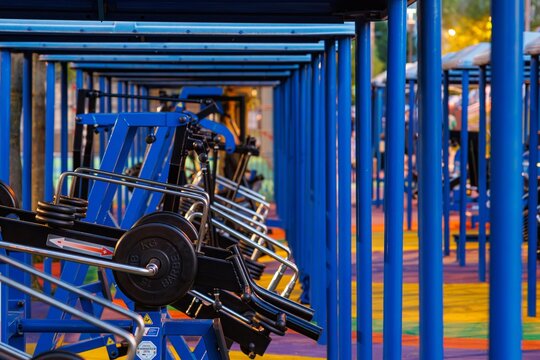 Rows of outdoor gym equipment set in a vibrant park at twilight, inviting people to exercise and enjoy the scenery. - Powered by Adobe